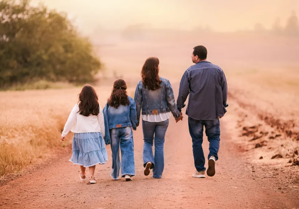 Une famille de quatre personnes marche dans un champ au soleil couchant